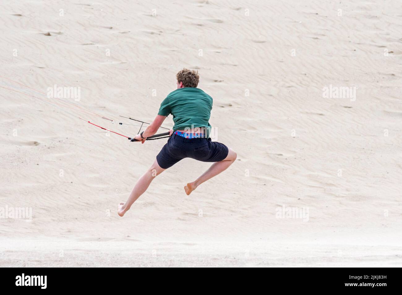 Jeune homme manipulant 4 lignes barre de contrôle d'un entraîneur de vol de quatre lignes parafoil / 4 lignes stunt kite sur la plage de sable dans le vent fort en été Banque D'Images