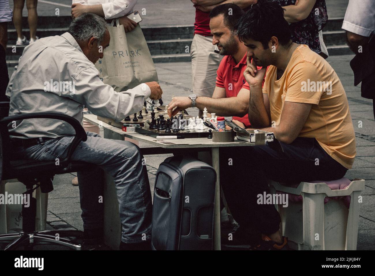An old man playing two games of chess simultaneously against younger men in one of the streets of Germany Banque D'Images