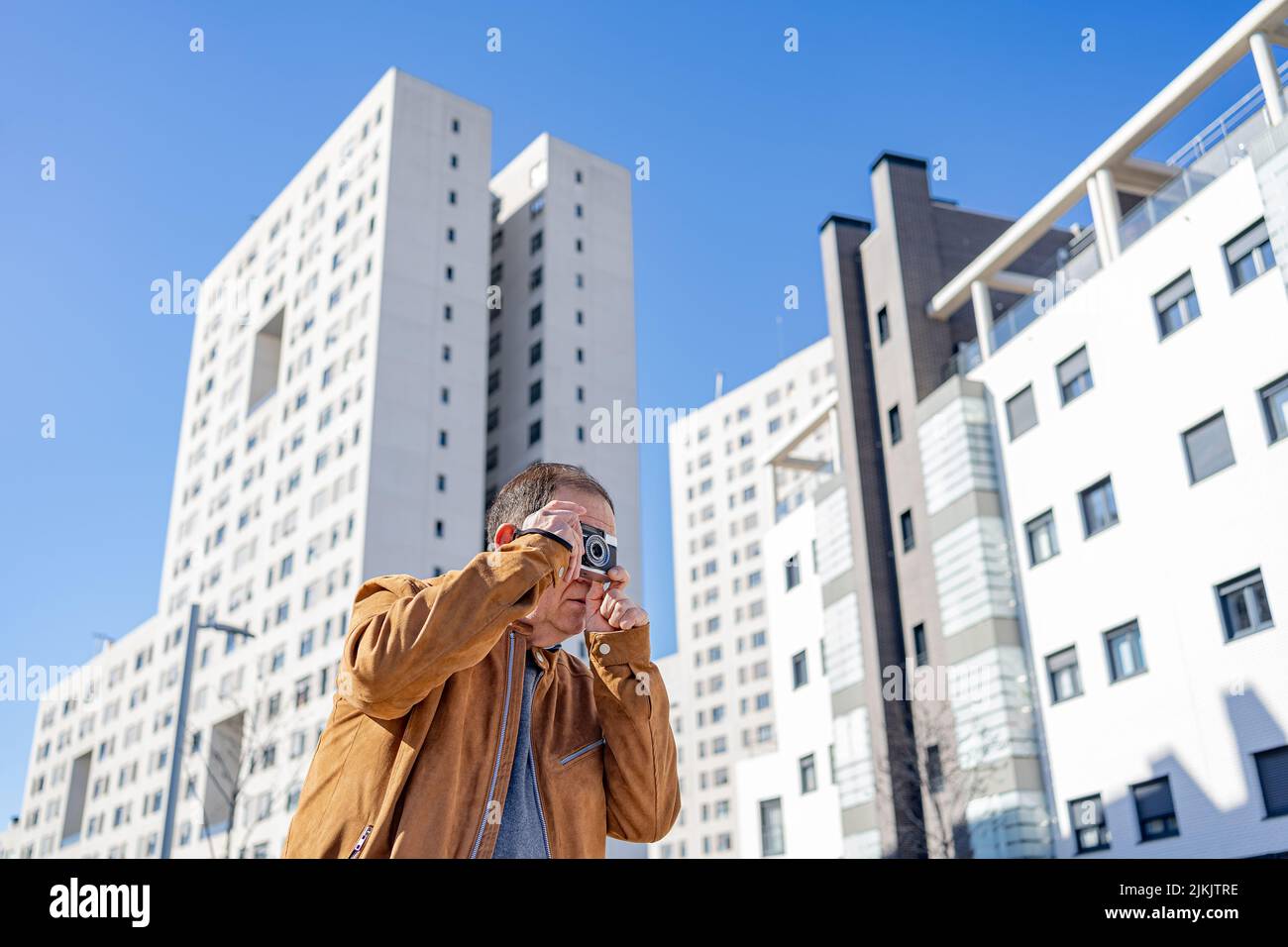 Un homme plus âgé qui photographie avec un vieux caméscope dans la ville avec des bâtiments en arrière-plan. Banque D'Images