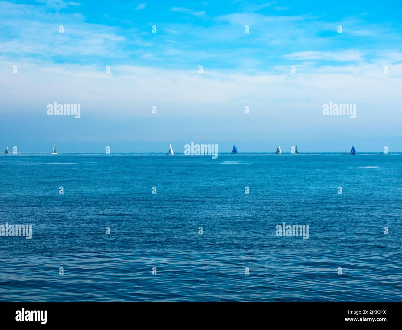 le soleil éclatant du matin illumine la mer et le ciel d'un bleu intense. à l'horizon, voiles blanches et voiles bleues Banque D'Images