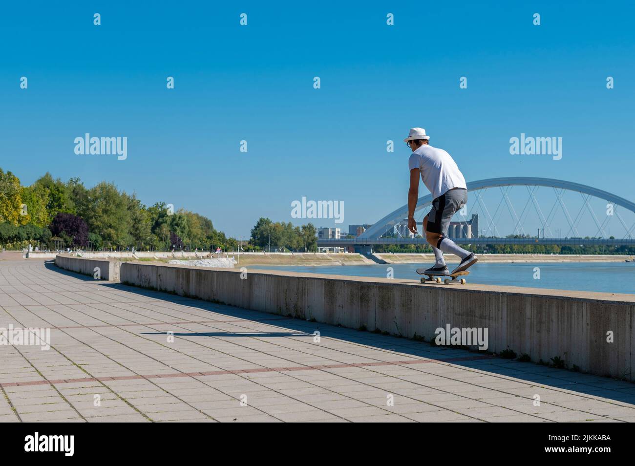 Un skateboarder caucasien conduisant sur une barrière en arrière-plan d'un lac Banque D'Images