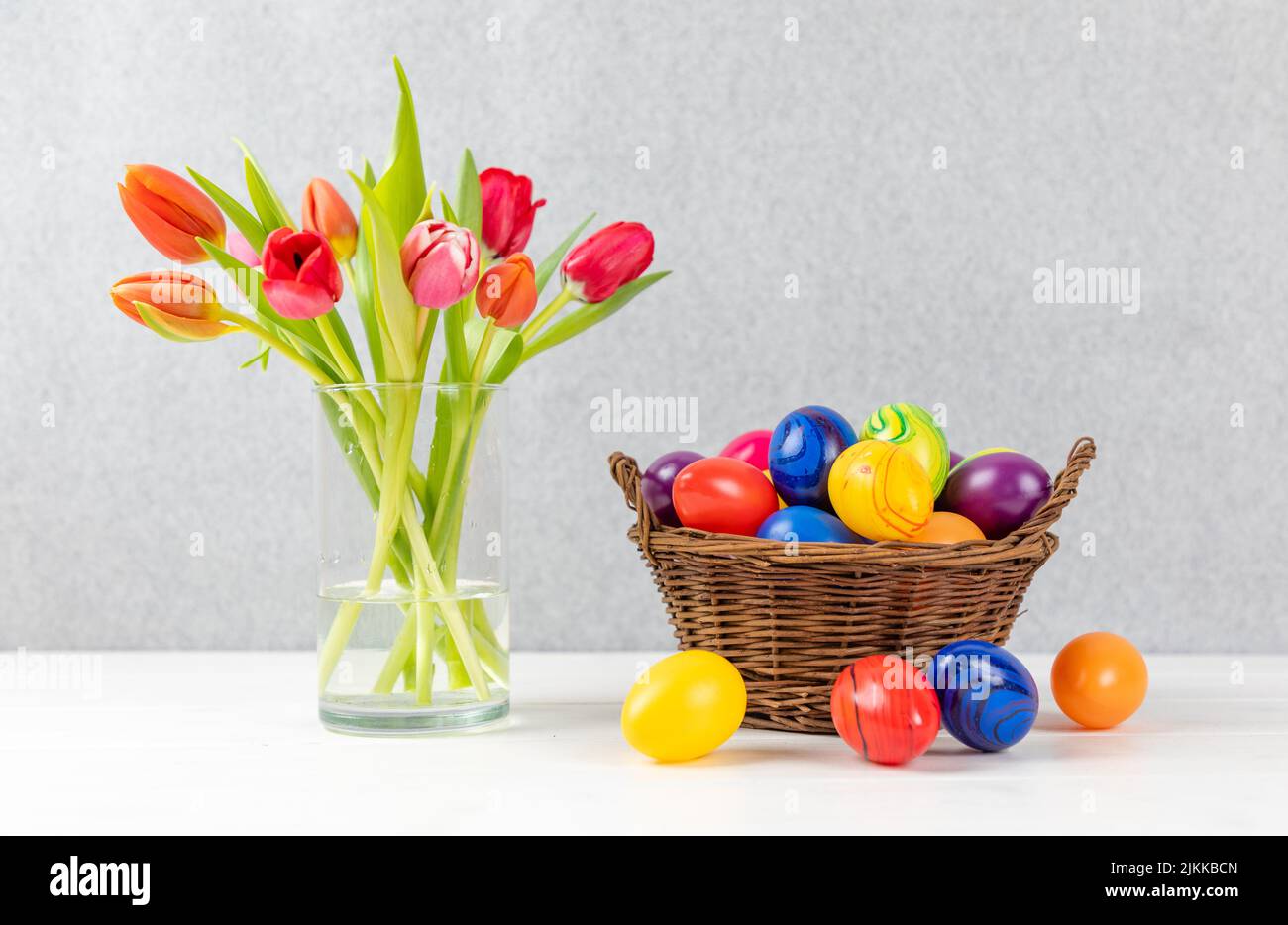 Tulipes colorées dans un vase avec œufs de pâques dans un panier à fond gris Banque D'Images