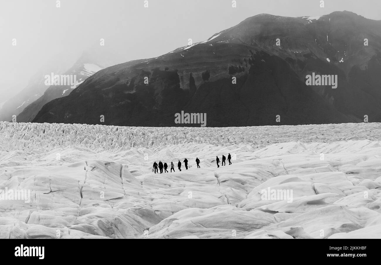 Une photo en noir et blanc d'un groupe de randonneurs marchant dans une zone montagneuse avec des montagnes boisées en arrière-plan Banque D'Images