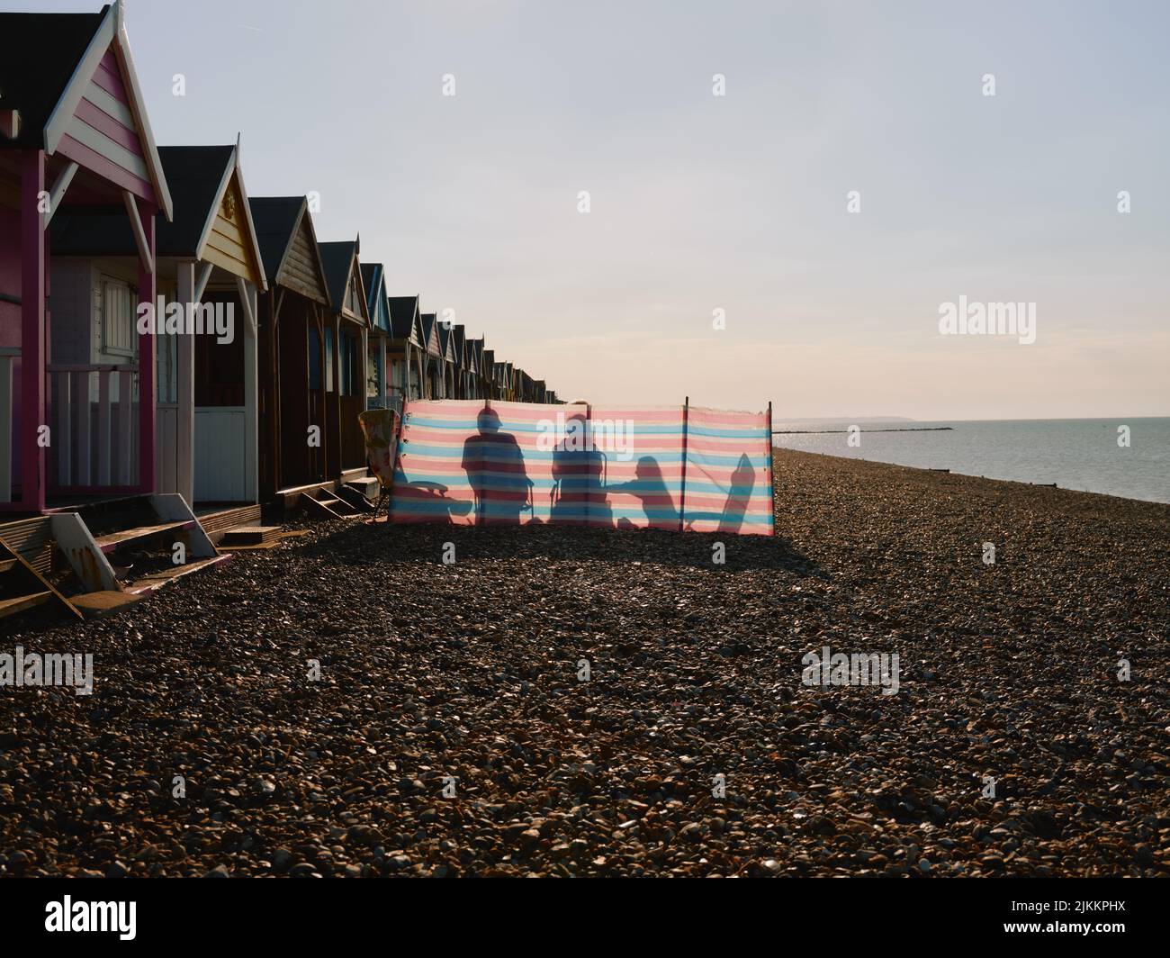 Plage d'été, cabanes de plage, coupe-vent et famille le jour d'été sur la plage de galets de Herne Bay, côte nord du Kent, Angleterre, Royaume-Uni - bord de mer de piété Banque D'Images