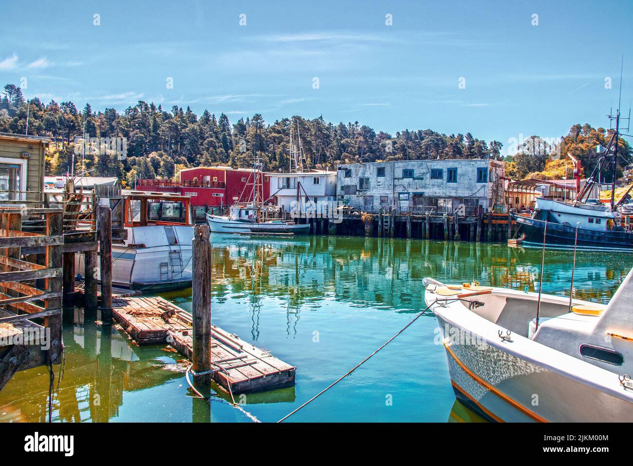 Bateaux de pêche amarrés dans le vieux port en activité et les quais avec des bâtiments décrépits reflétés dans l'eau turqoise à ft. Bragg, Californie, États-Unis Banque D'Images