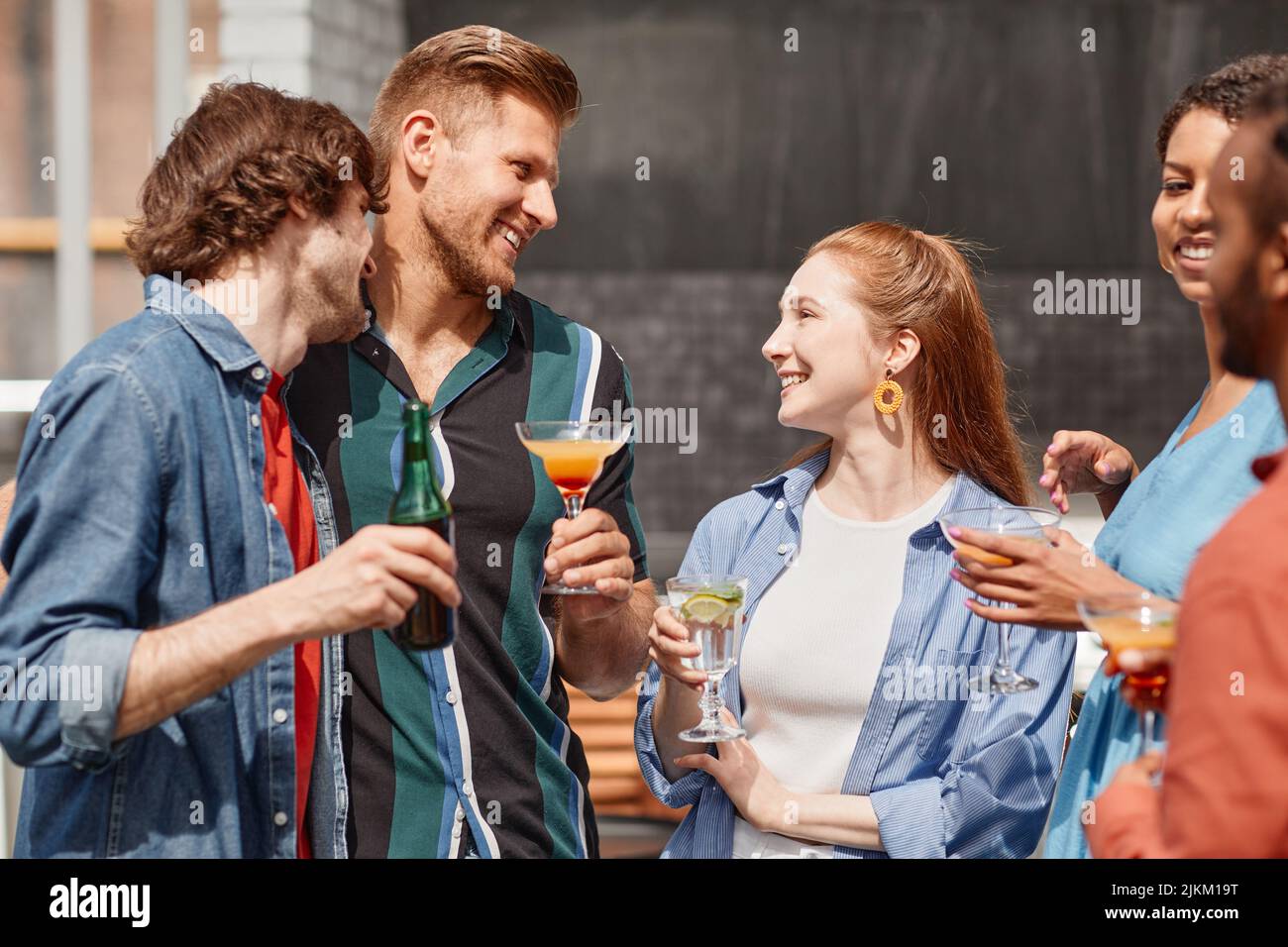 Portrait de deux jeunes hommes prenant un verre à la fête en plein air avec des amis en plein soleil Banque D'Images