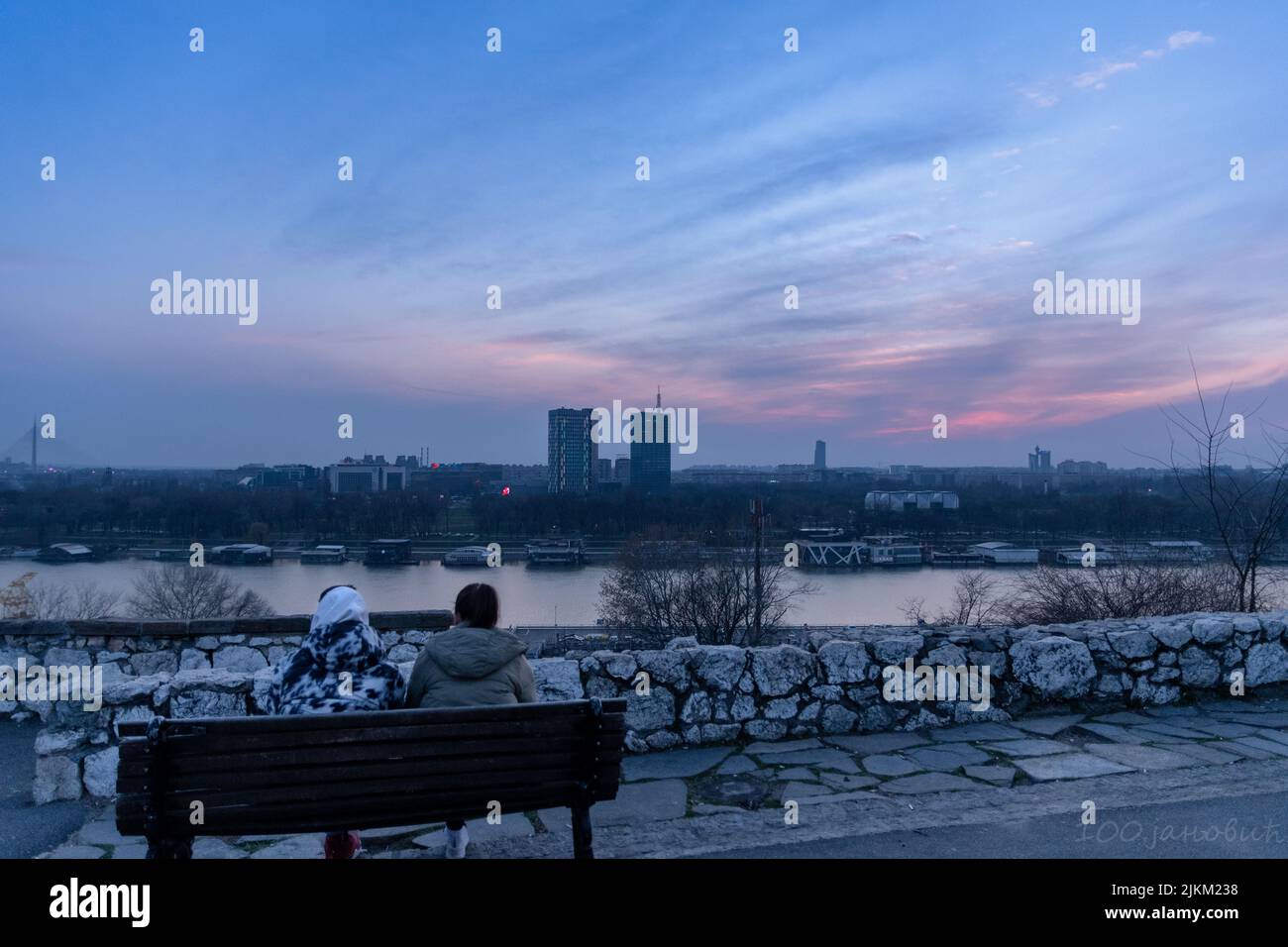 A back view op a couple sitting on the bench near the lakeshore on a sunset sky background Banque D'Images