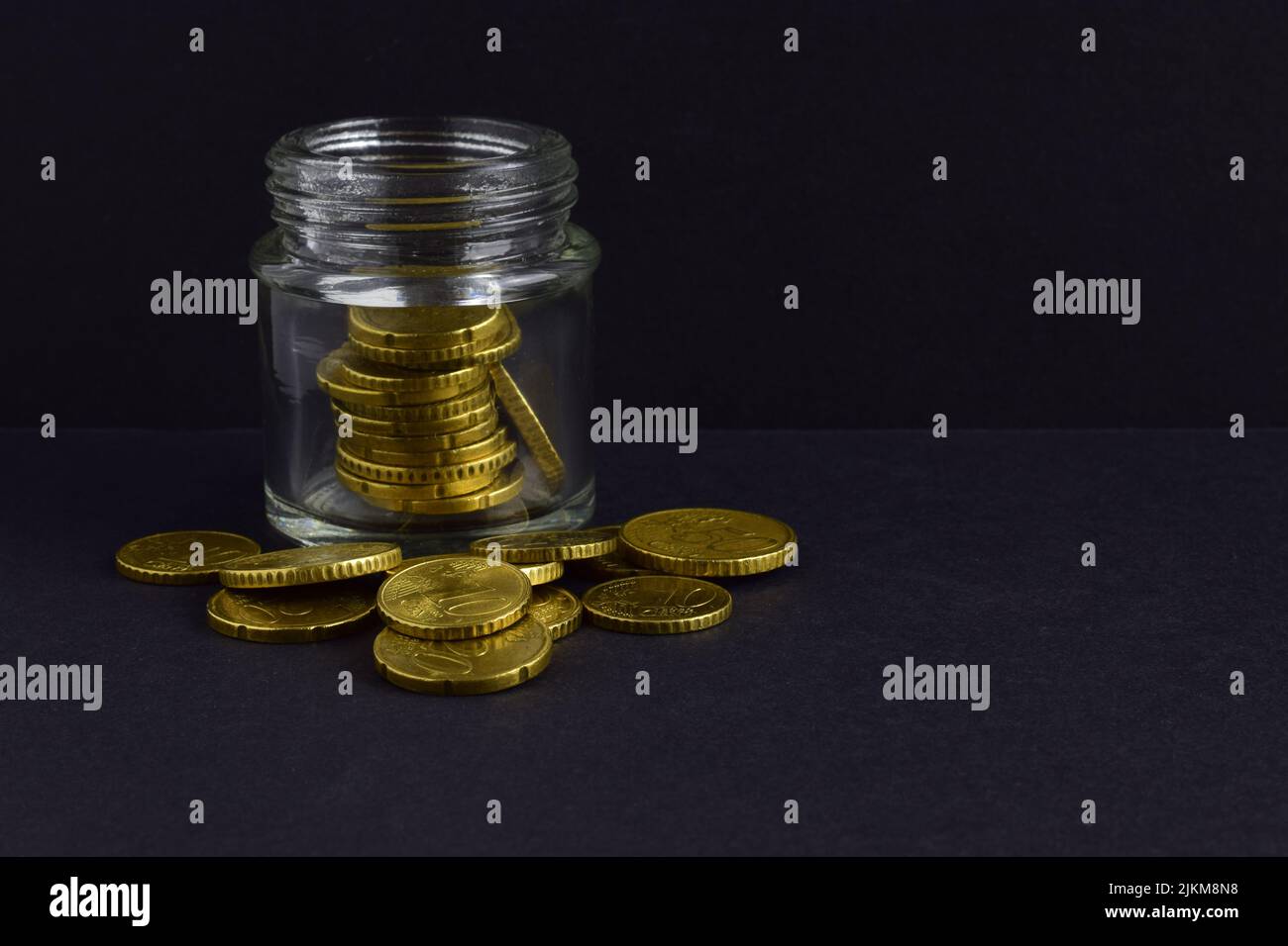 Les pièces en euros sont dispersées et dans le pot de verre isolé sur un fond noir Banque D'Images