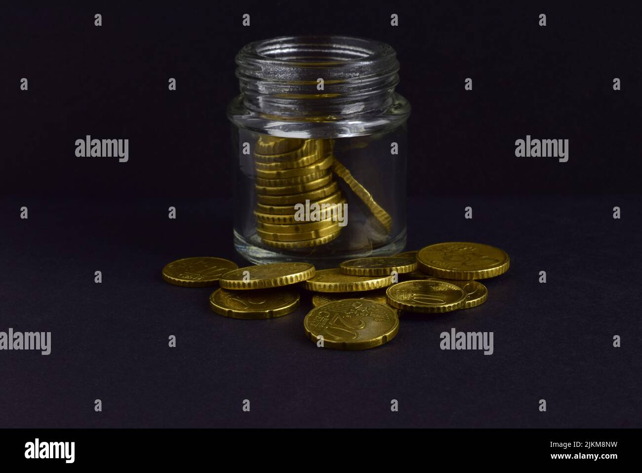 Gros plan d'un pot en verre rempli de pièces de monnaie et de pile de pièces de monnaie autour d'elle sur un fond gris Banque D'Images