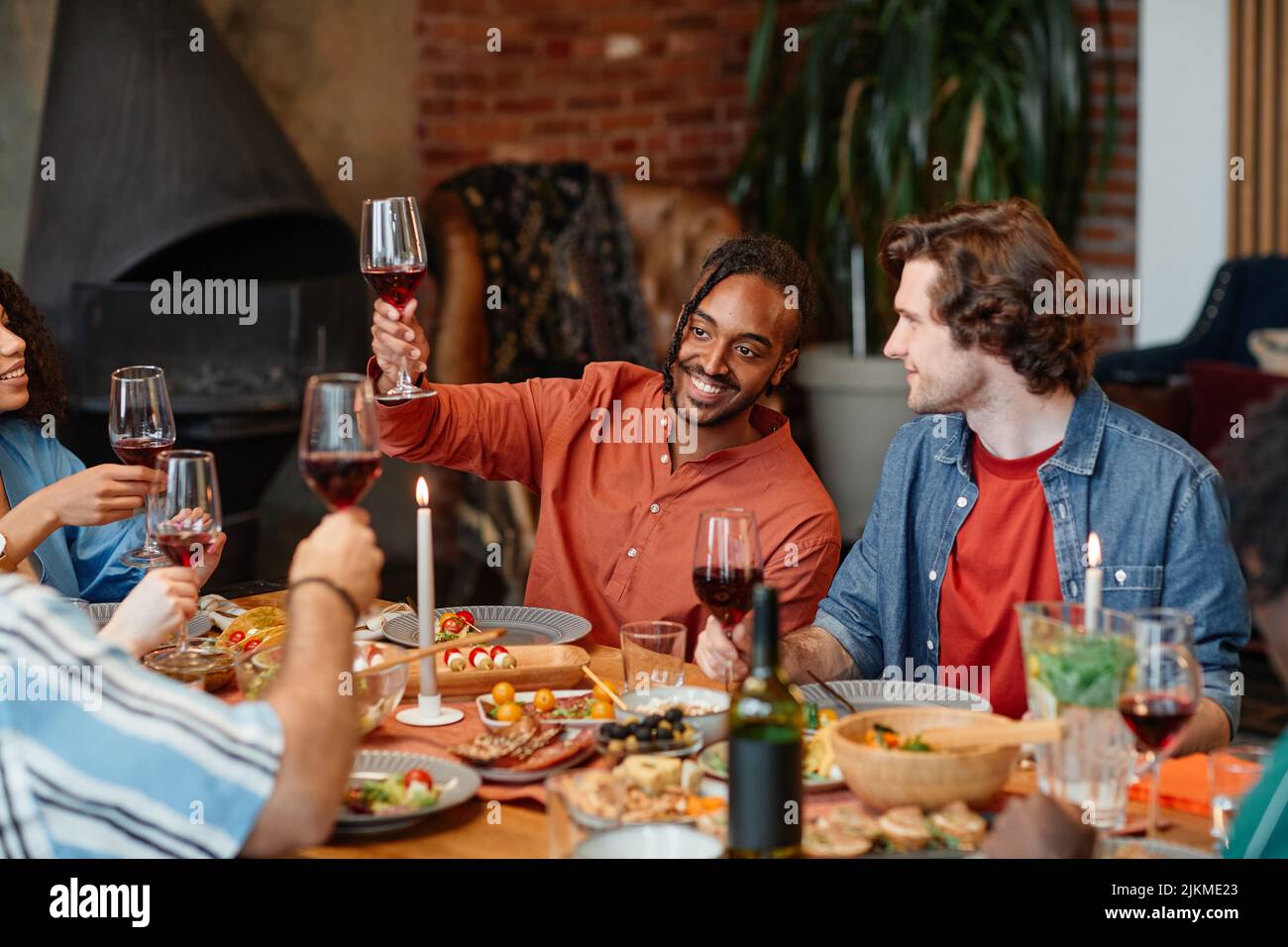 Portrait d'homme noir souriant en train de griller avec des lunettes de vin pendant le dîner avec des amis dans un cadre confortable Banque D'Images