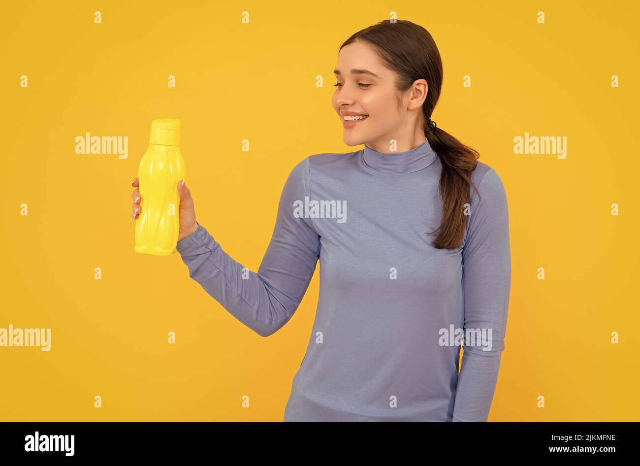 une femme souriante tient de l'eau minérale. elle a soif. jeune femme avec une bouteille de sport en plastique. Banque D'Images