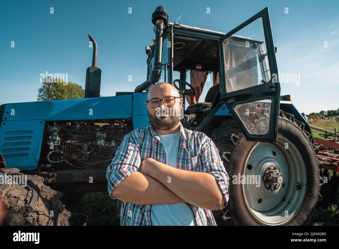 Portrait du conducteur du tracteur satisfait après le travail sur le terrain agricole se trouve à côté du tracteur. Agriculture et récolte. Banque D'Images