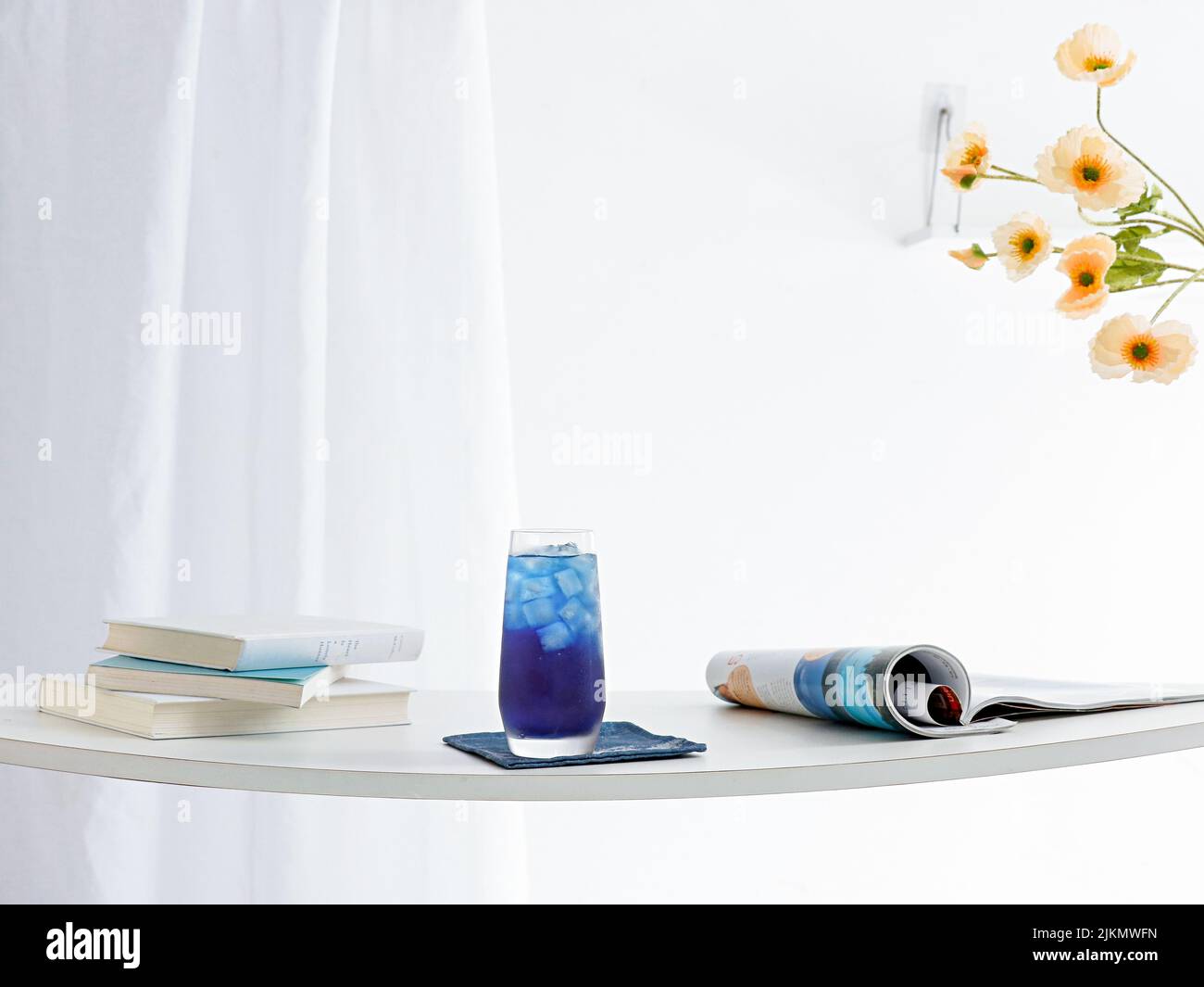 Un verre de boisson bleue rafraîchissante et des journaux sur une table avec des rideaux blancs en arrière-plan Banque D'Images