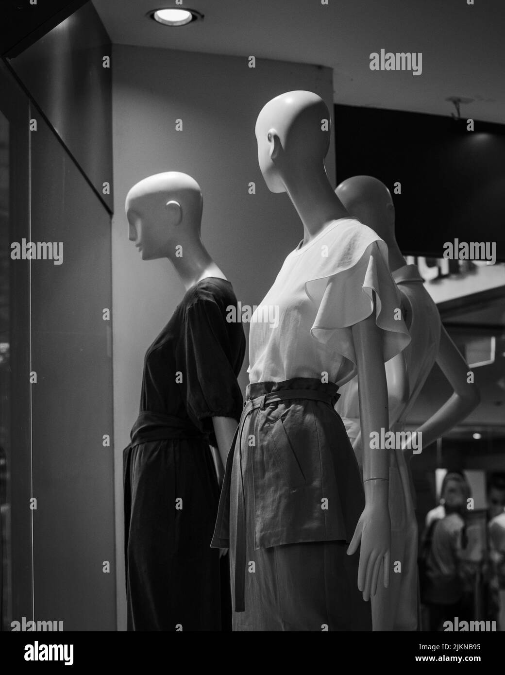 Une photo en échelle de gris de trois mannequins d'habillement pour femmes dans une boutique de vêtements Banque D'Images
