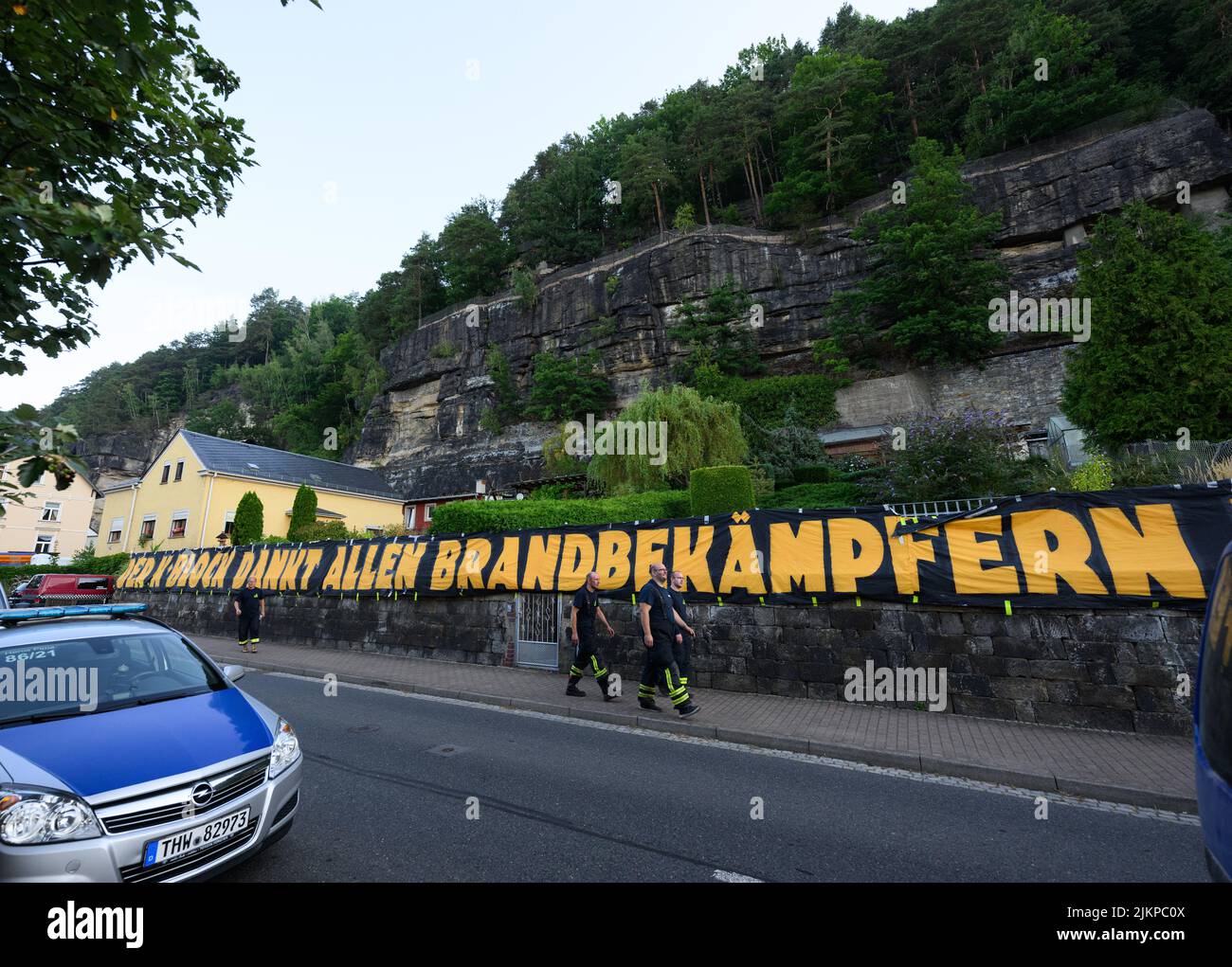 Bad Schandau, Allemagne. 03rd août 2022. Les pompiers marchent sur une bannière « le bloc K remercie tous les pompiers » près du centre des opérations pour avoir combattu les feux de forêt dans le parc national de la Suisse saxonne ce matin. Avec la bannière, les Ultras de la troisième division équipe de football SG Dynamo Dresden remercie les aides dans la zone de feu de forêt. Crédit : Robert Michael/dpa/Alay Live News Banque D'Images