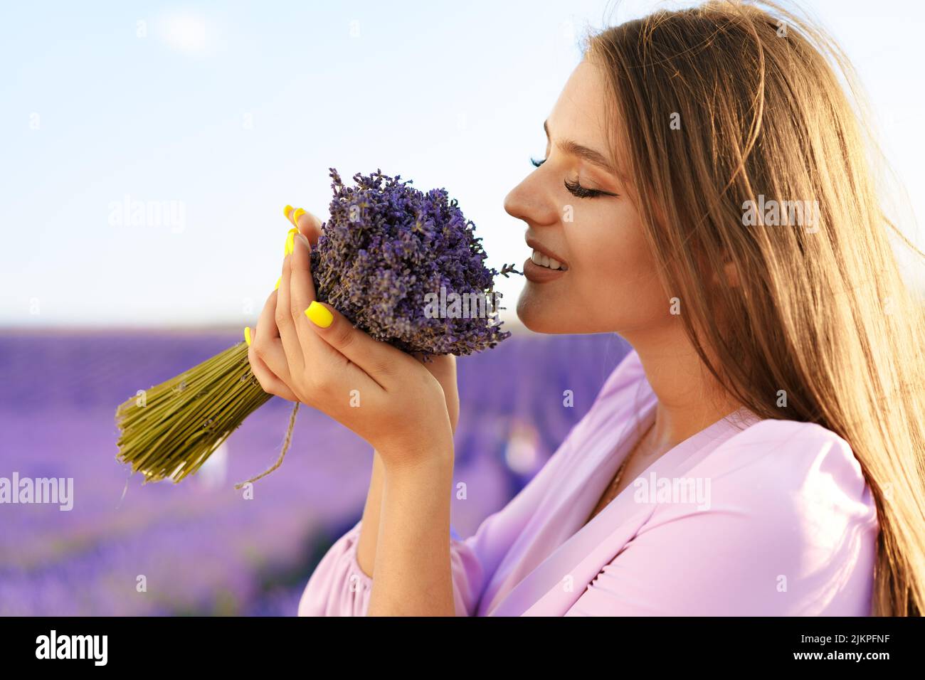 Jeune femme en robe tenant un bouquet de fleurs debout dans le champ de lavande Banque D'Images