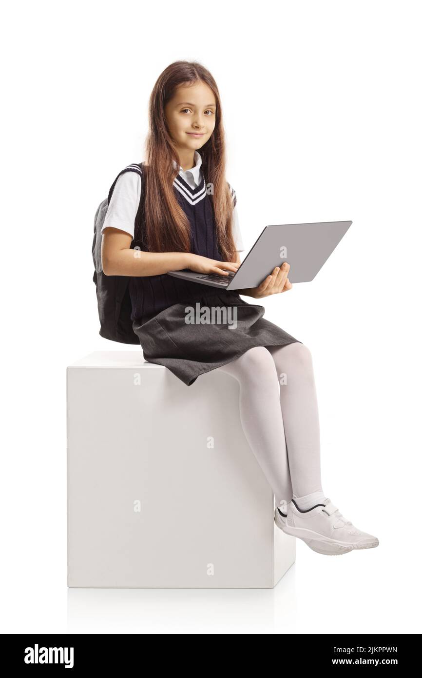 Petite écolière souriante assise avec un ordinateur portable isolé sur fond blanc Banque D'Images