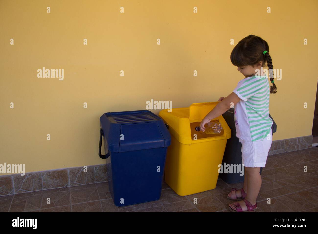 adorable petite fille jetant une bouteille d'eau dans une poubelle. Référence à l'éducation des enfants au respect de la nature et au recyclage Banque D'Images