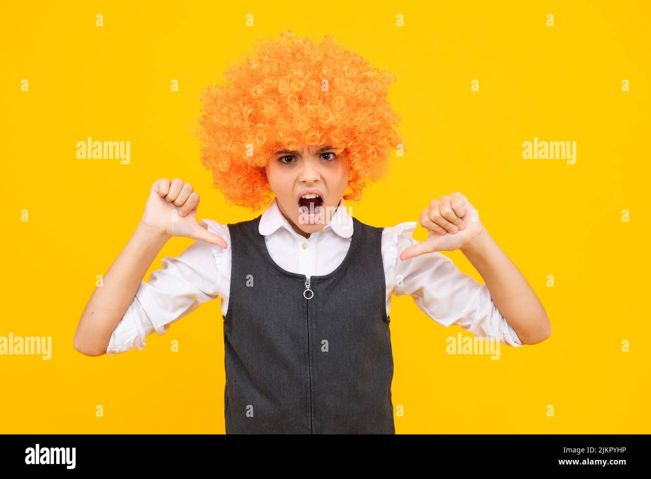 Anniversaire fête d'enfants. Drôle d'enfant dans la perruque clown curly isolé sur fond jaune. Adolescente en colère, contrariée et malheureuse émotion négative. Banque D'Images