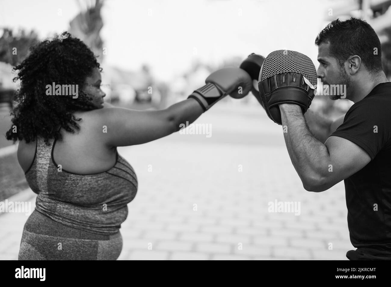 Femme africaine curvy et entraîneur personnel faisant la séance d'entraînement de boxe en extérieur - Focus sur l'homme gant - montage noir et blanc Banque D'Images