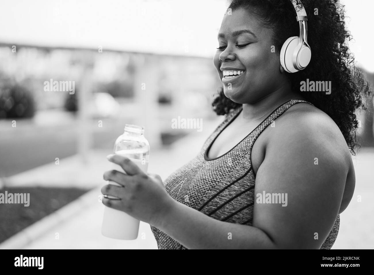 Femme curvy buvant de l'eau pendant la routine de jogging extérieur - Focus sur les écouteurs - montage noir et blanc Banque D'Images