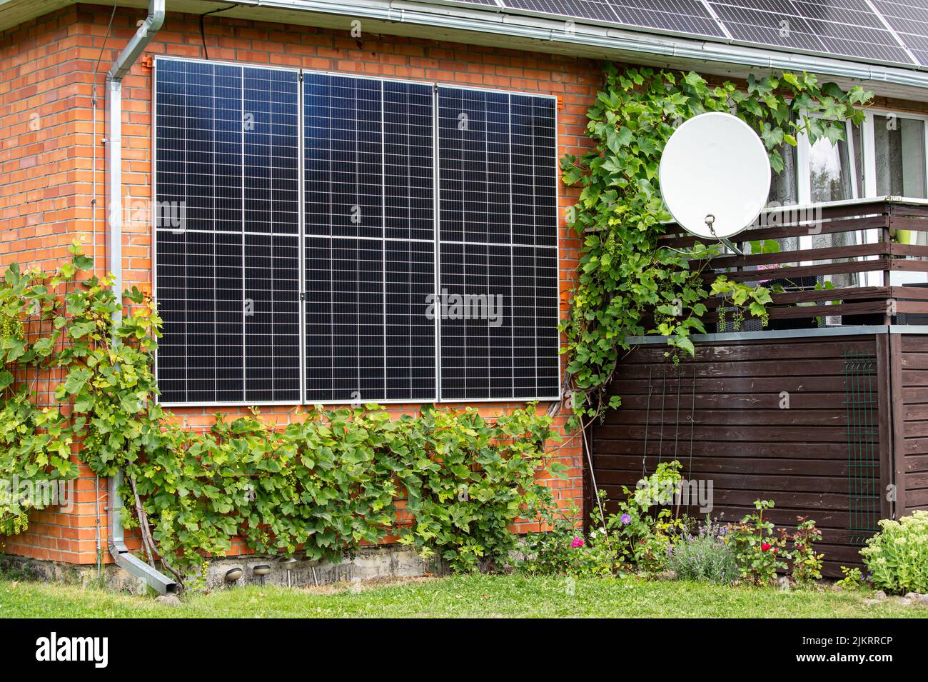 Panneaux solaires fixés à une maison domestique pour économiser de la pièce et produire de l'énergie verte. Beau jardin avec vignes et fleurs qui poussent. Banque D'Images