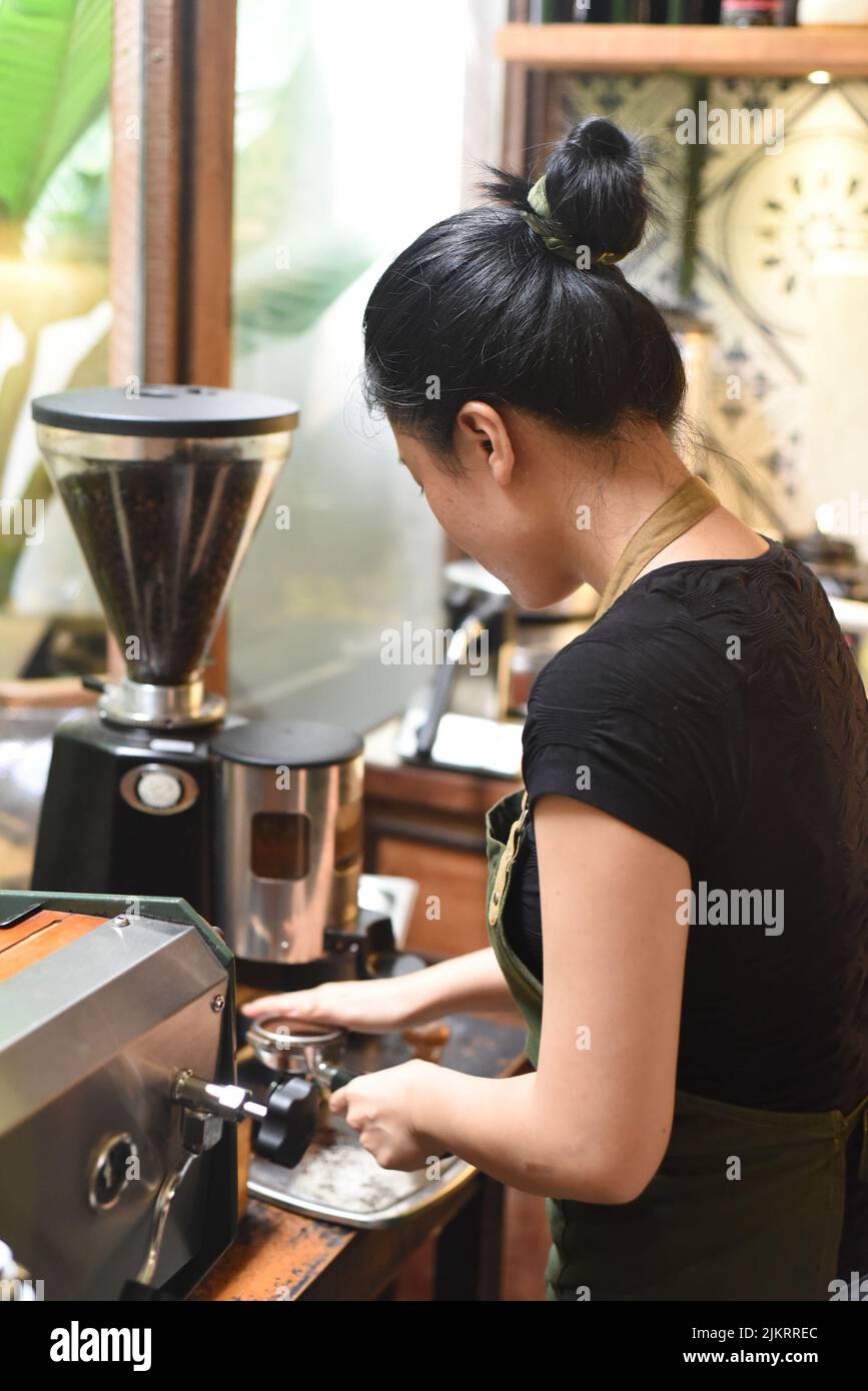 Une serveuse vietnamienne fait du café via le porte-filtre d'une machine à café Banque D'Images