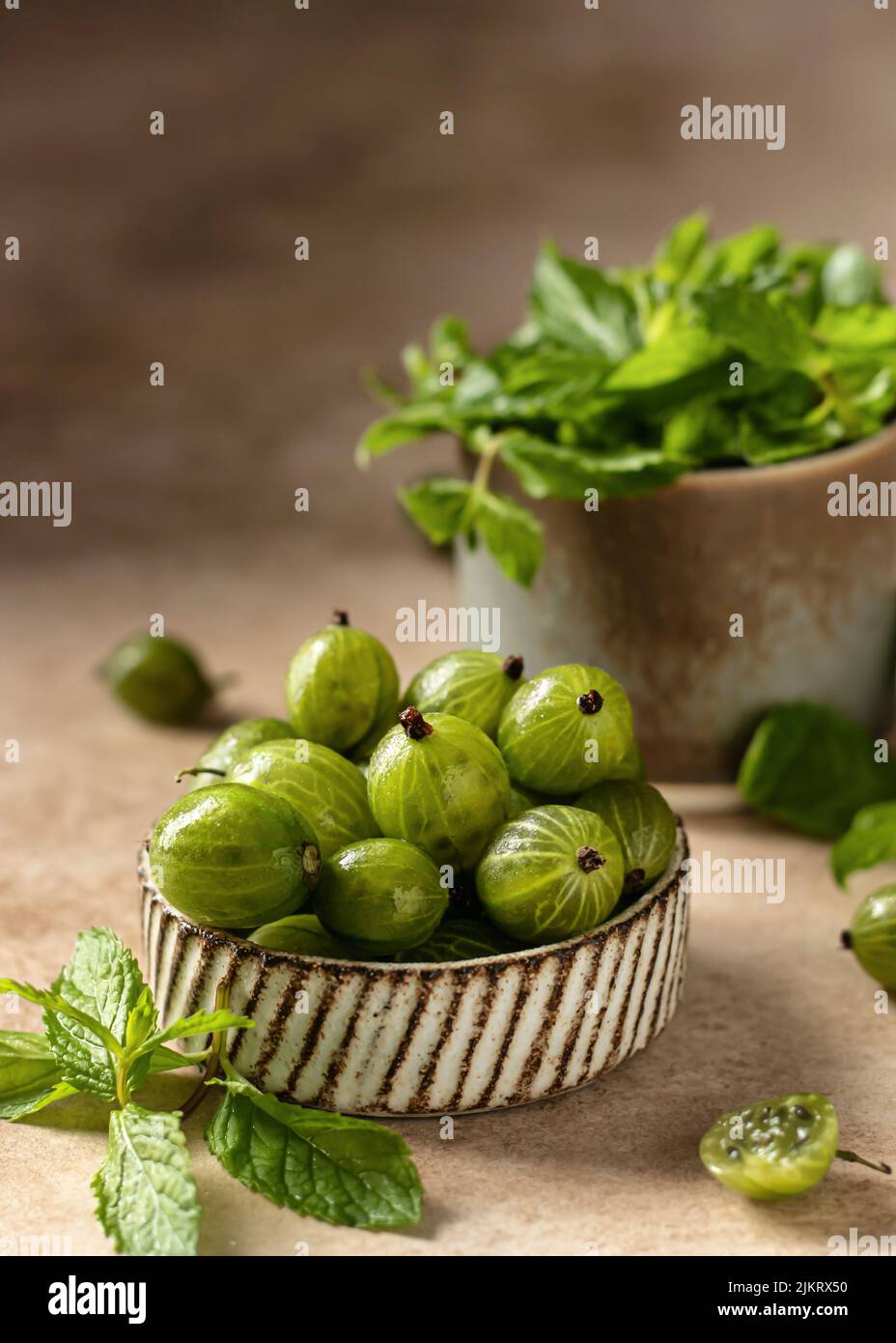 Groseille fraîche dans un bol en céramique avec feuilles de menthe sur fond beige texturé avec espace de copie. Gros plan. Dessert cru sain. Banque D'Images