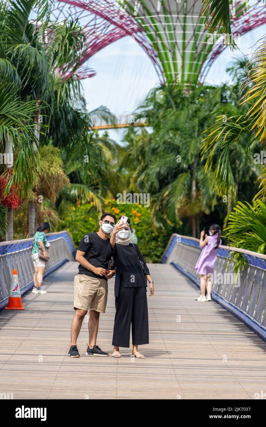 Un couple malais portant un parasol prend des photos de selfie sur le pont avant de se rendre à Gardens by the Bay. Singapour 2022. Banque D'Images