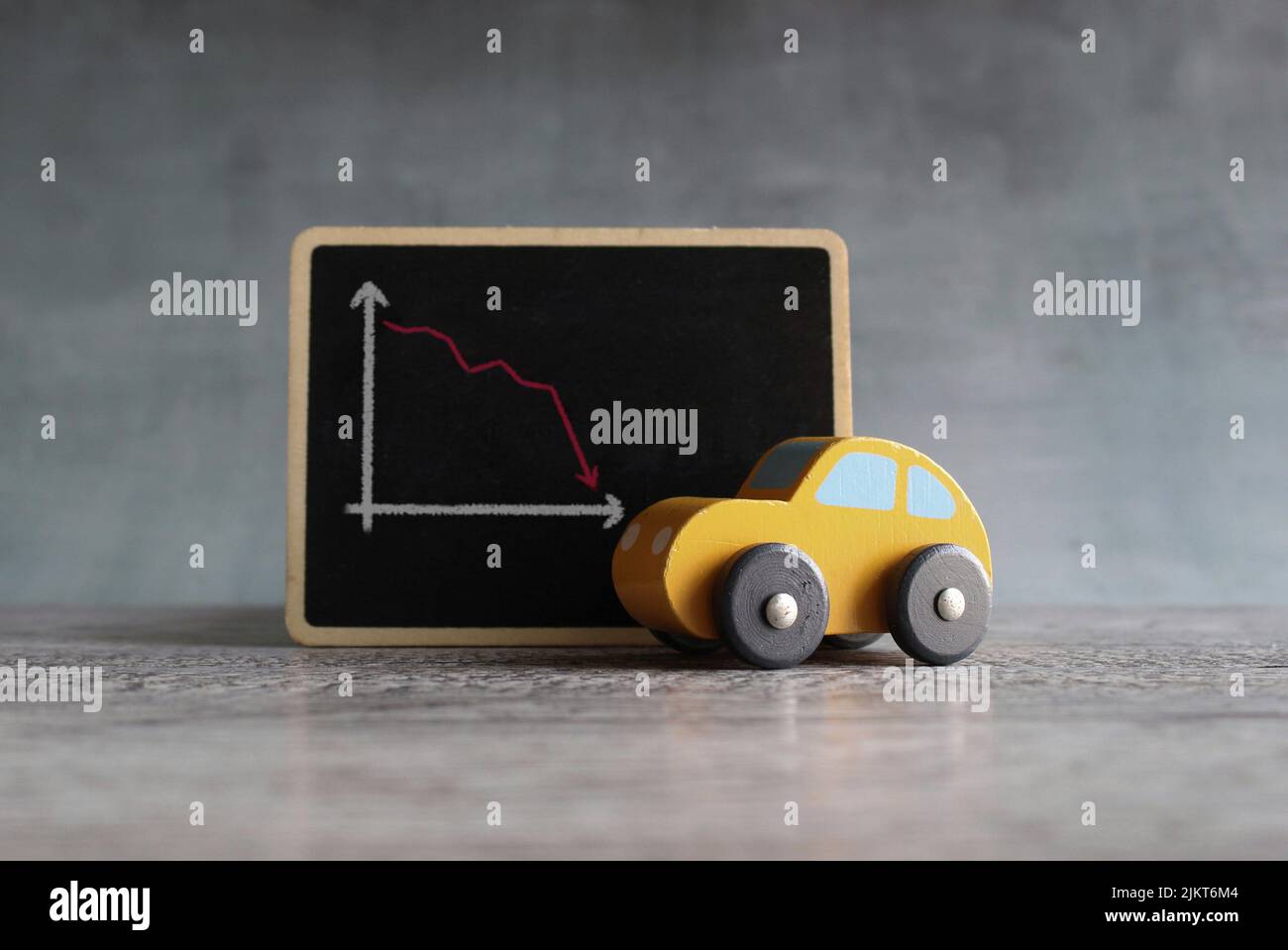 Voiture-jouet et tableau noir avec flèche vers le bas. Le concessionnaire de location de voitures réduit le concept de perte de ventes. Banque D'Images