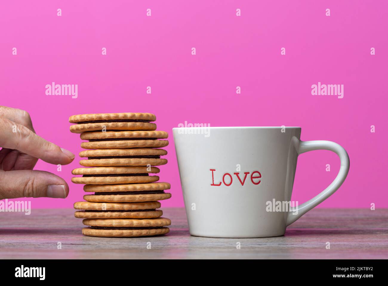 Main prenant un biscuit d'une pile à côté d'une tasse avec "amour" écrit dessus. Banque D'Images