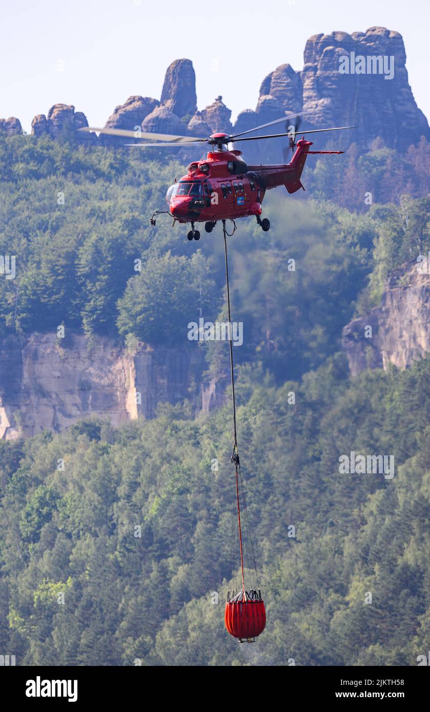 Bad Schandau, Allemagne. 03rd août 2022. Un hélicoptère cargo en provenance d'Autriche vole avec un réservoir d'eau externe pour éteindre un feu de forêt dans le parc national de la Suisse saxonne. Crédit : Robert Michael/dpa/Alay Live News Banque D'Images