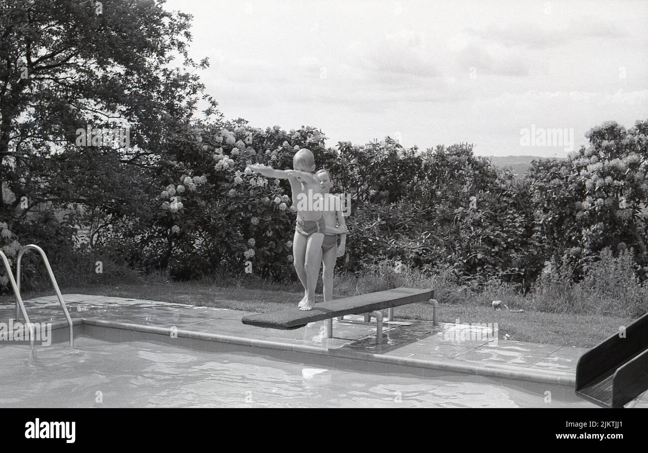 1960s, historique, à l'extérieur dans un jardin, deux jeunes garçons dans une piscine extérieure en plein air, un sur le plongeoir, Angleterre, Royaume-Uni. Banque D'Images