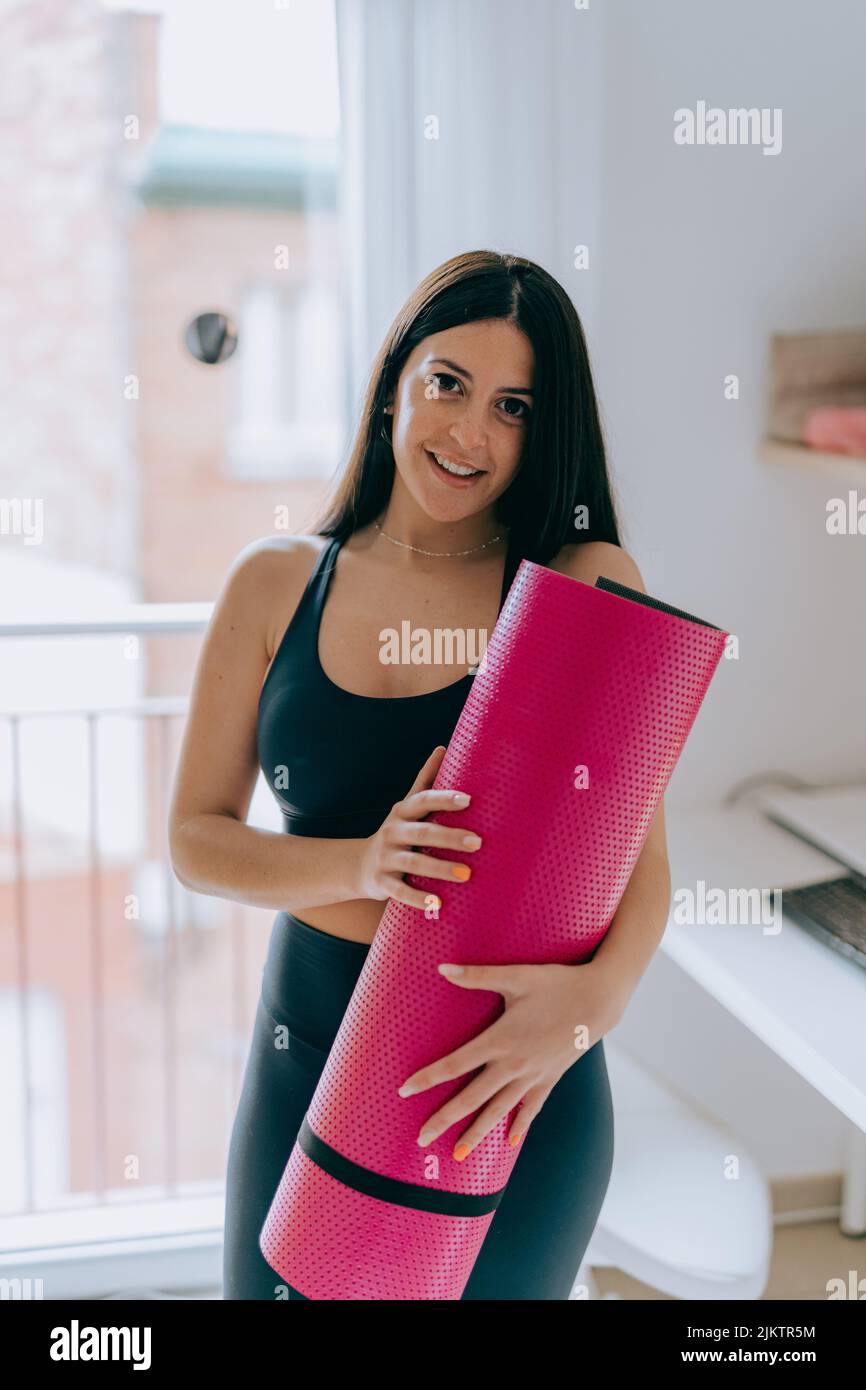 Un cliché vertical d'une femme hispanique dans ses vêtements de sport, portant un tapis de yoga rose Banque D'Images