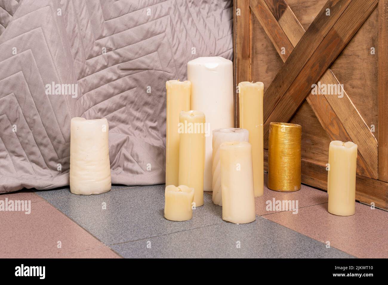 Un petit groupe de bougies de différentes formes, tailles et couleurs se dresse au sol de la chambre à coucher près du lit et de la table de chevet. Banque D'Images