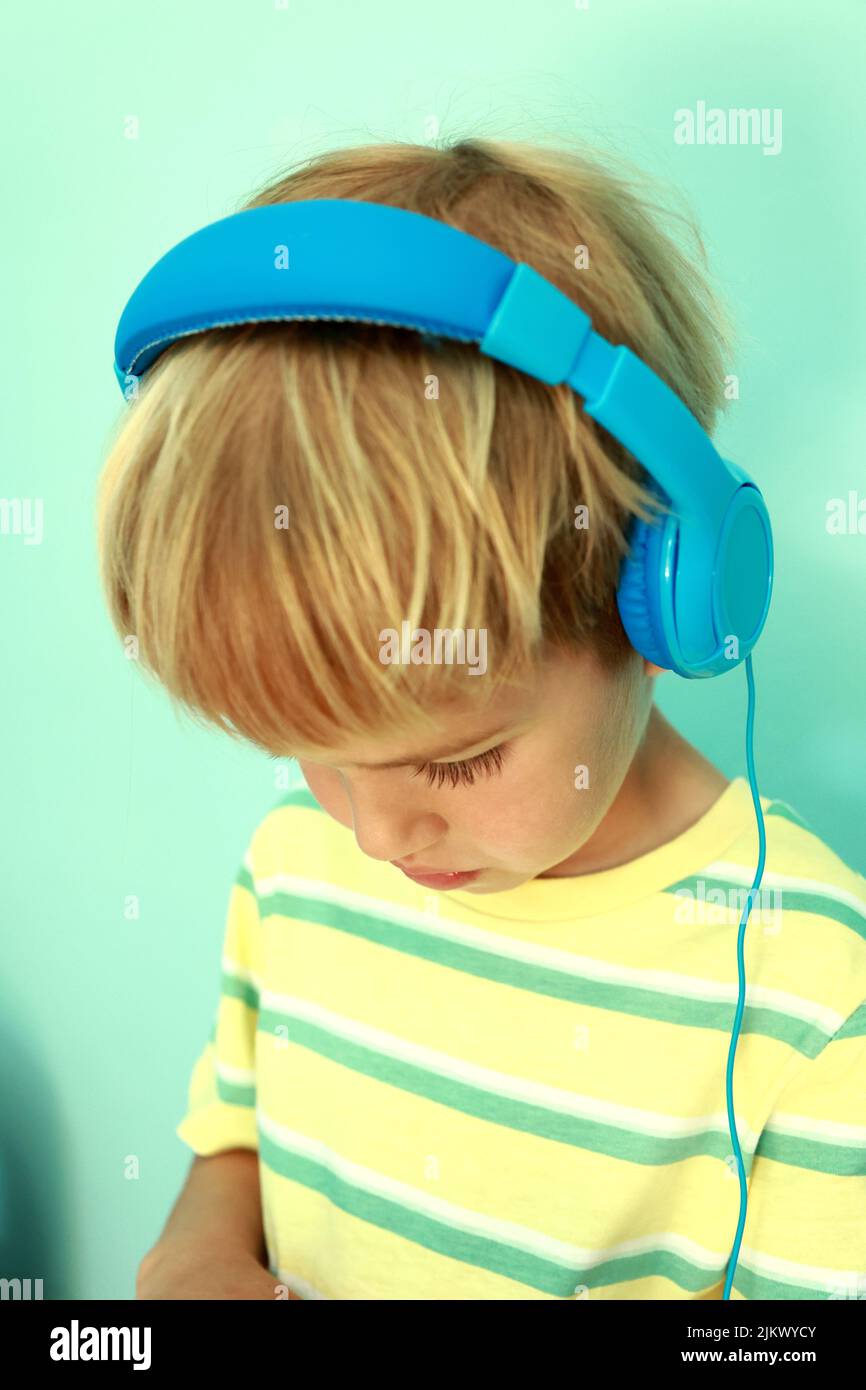 Adorable petit garçon concentré de 5s ans, portant un casque bleu, regardant la tablette. Petit garçon avec un casque jouant à l'appareil de jeu Banque D'Images