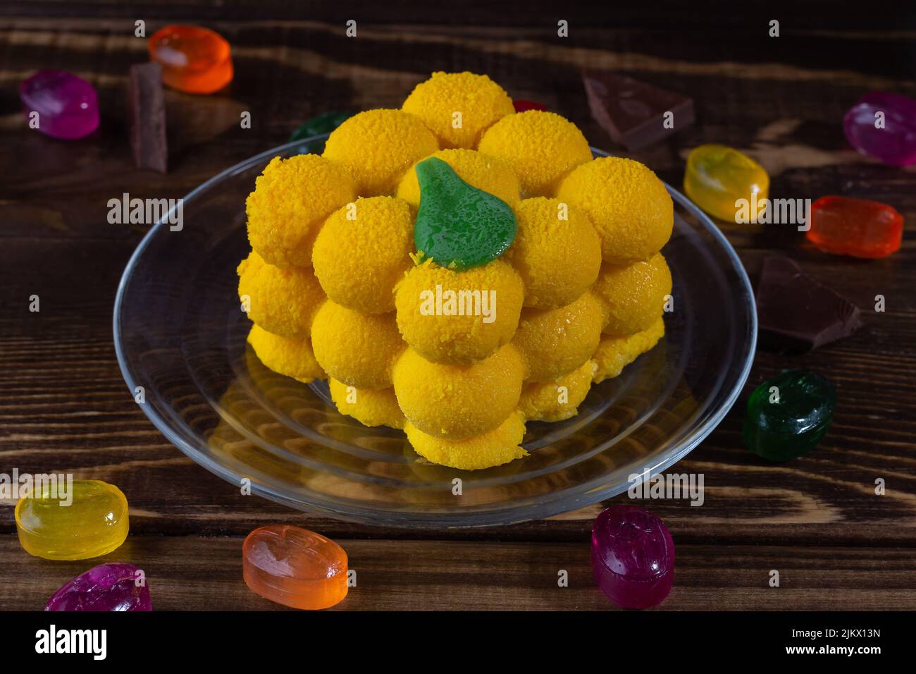 Appétissant et attrayant gâteau à la mousse de mangue jaune sur une table en bois sombre avec des bonbons et des chocolats épars, mise au point sélective. Banque D'Images