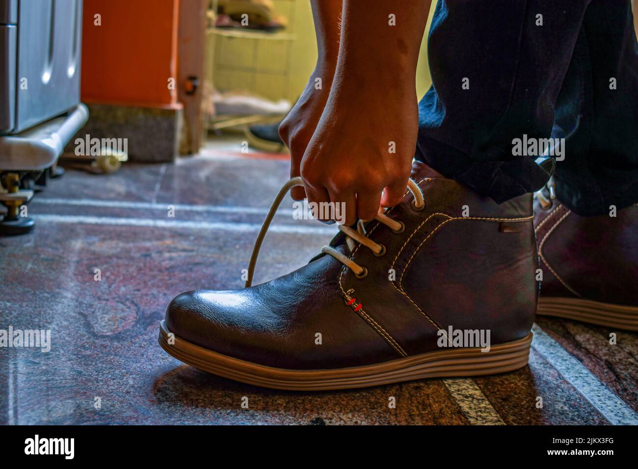 Photo de l'Indien portant une chaussure de couleur marron foncé et une dentelle de chaussure nouant, se préparer pour son bureau. Photo prise sous lumière naturelle à Ban Banque D'Images