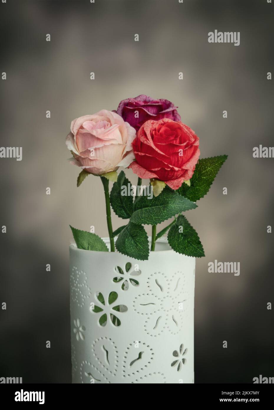 A vertical shot of three beautiful roses of different colors in a white ornamented vase Banque D'Images