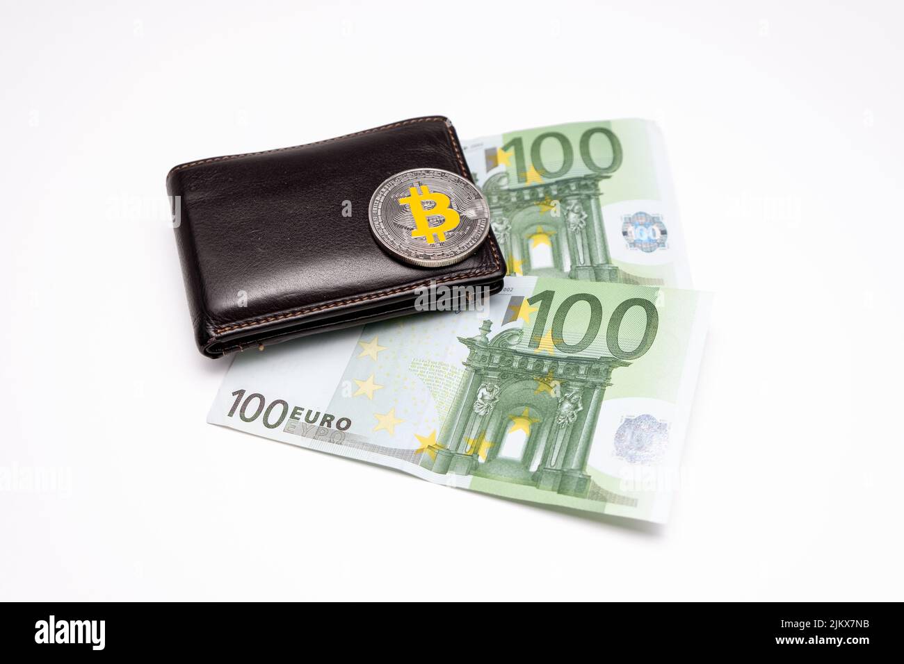 Pièce en bitcoin sur le dessus du portefeuille avec deux billets de 100 euros sur fond blanc. Bitcoin sur portefeuille avec deux cents billets de banque. Banque D'Images