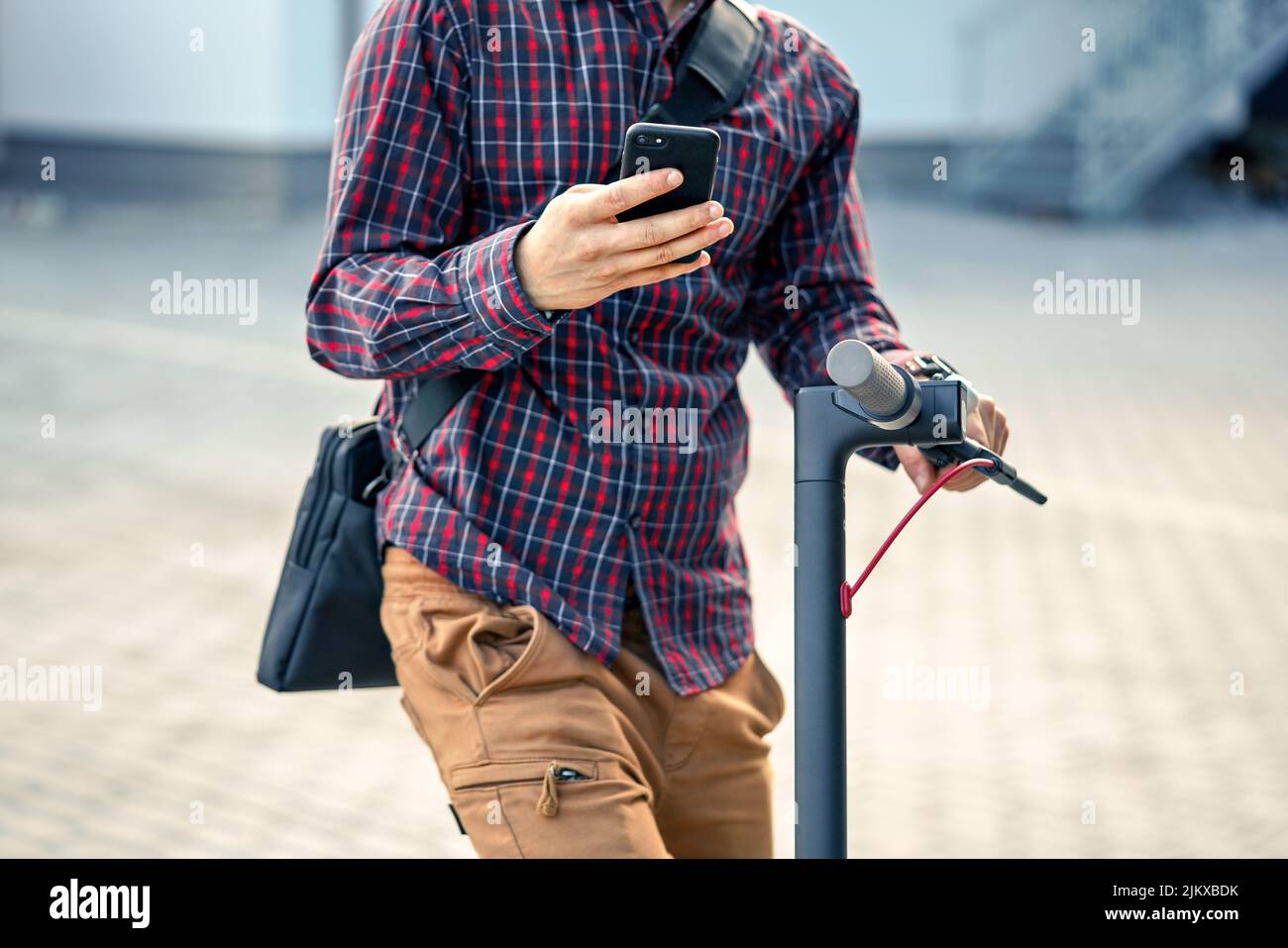 Jeune homme portant une chemise penchée sur un guidon de scooter électrique, tenant le smartphone mobile dans ses mains, détail gros plan Banque D'Images