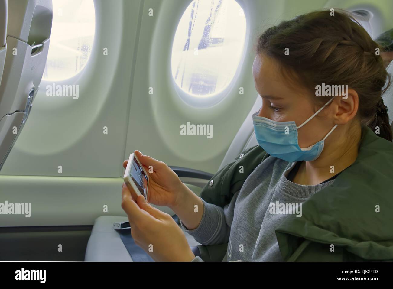 femme voyageur portant un masque facial pour prévenir l'infection par le covid-19 pendant le voyage en avion à l'aide d'un téléphone portable lorsqu'elle est assise dans l'avion. Banque D'Images