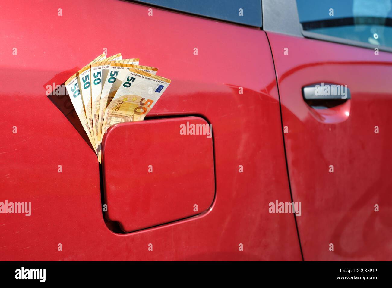 Cinquante billets d'euros qui sortent du réservoir de carburant fermé d'une voiture, ce qui augmente le prix du carburant. Banque D'Images