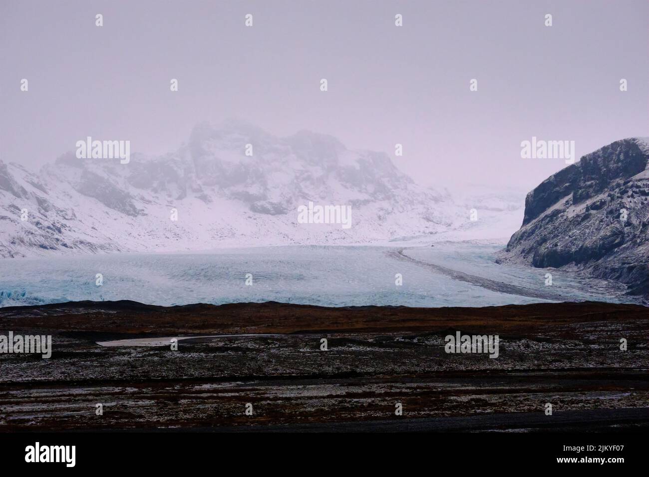 Glacier bleu entre deux montagnes au premier plan brun foncé. Banque D'Images