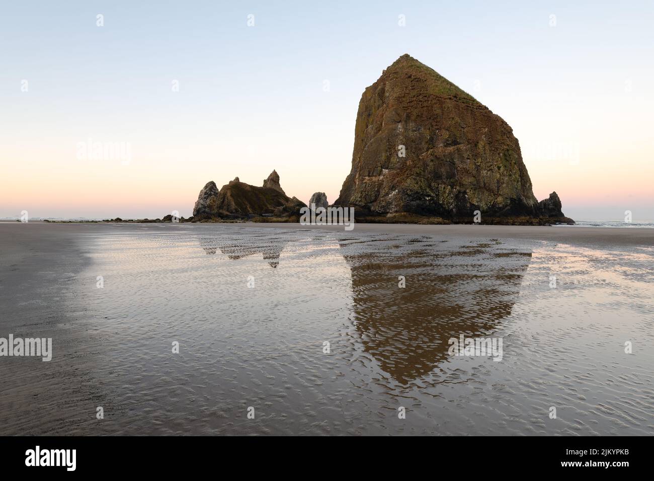 Aube au monolithe Haystack Rock à Cannon Beach, Oregon, avec une réflexion dans le sable humide avec des ondulations en début de matinée Banque D'Images