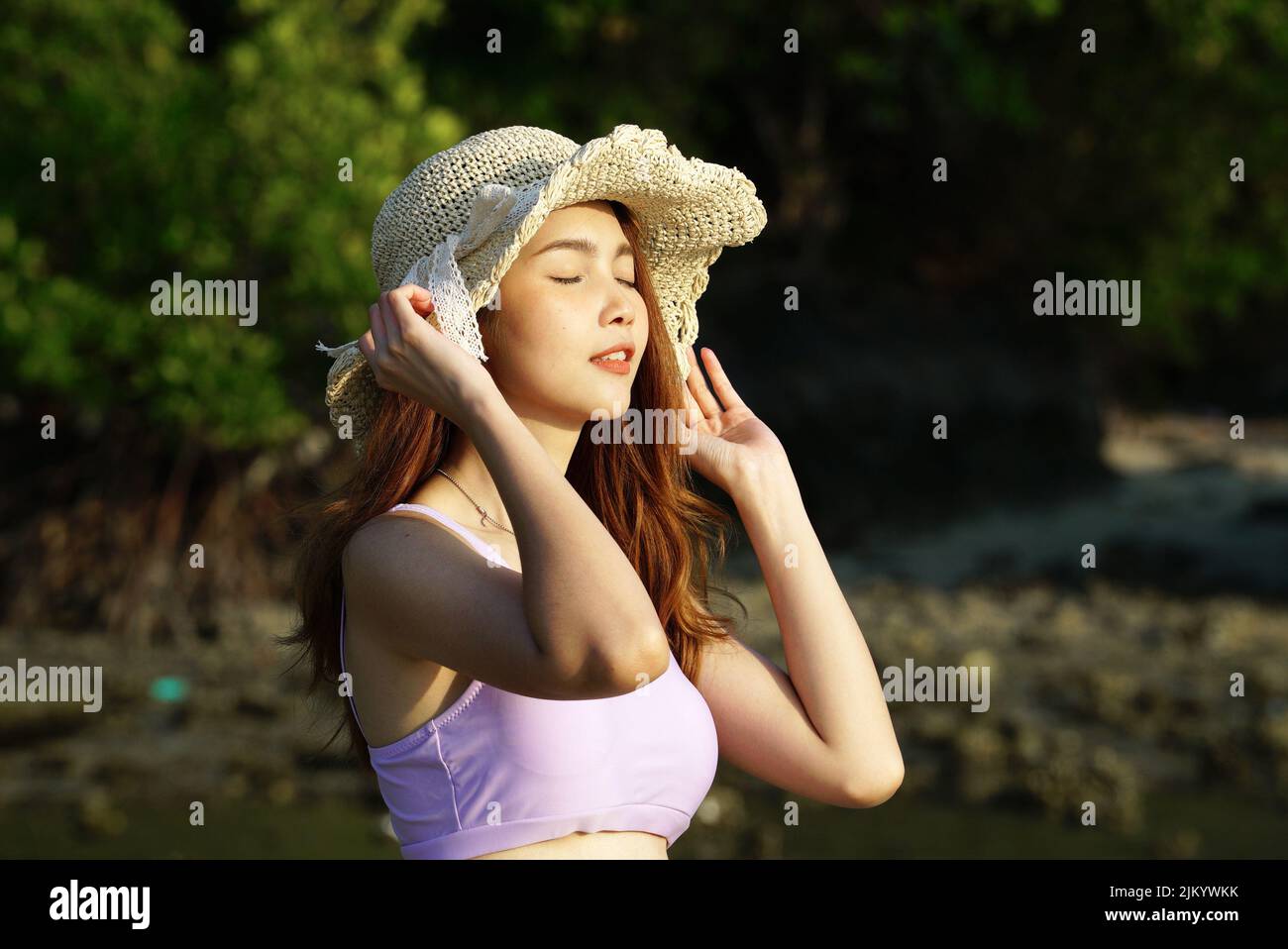 Une jolie femme sud-asiatique avec un chapeau contre les arbres sous la lumière du soleil Banque D'Images