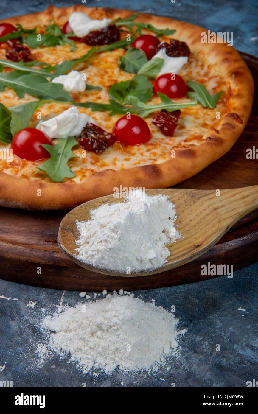 Un cliché sélectif de tarte à la pizza avec garnitures et une poudre de fromage blanc sur la louche en bois à côté Banque D'Images