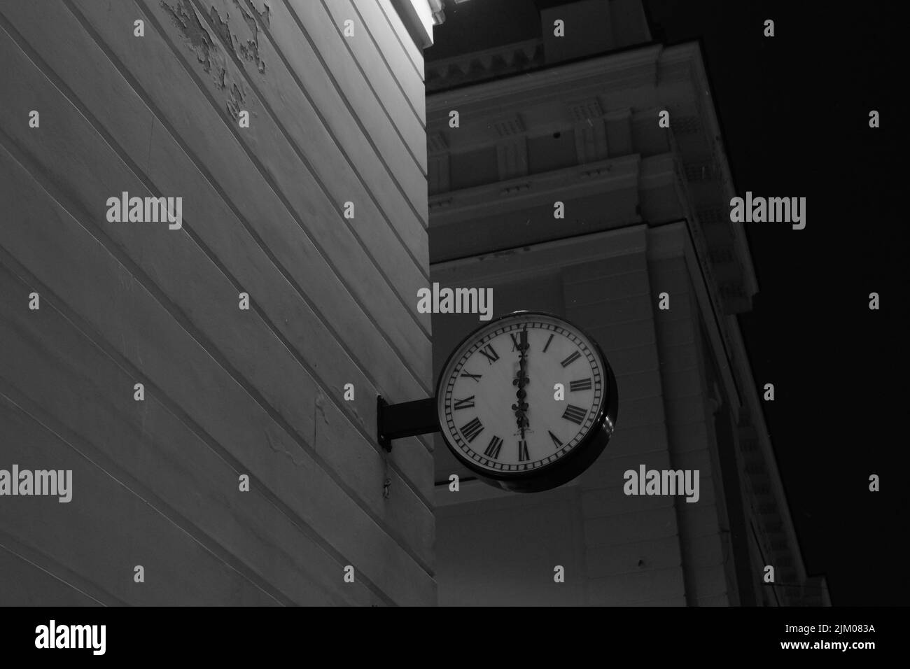 Photo d'une horloge en bas angle en niveaux de gris sur le côté d'un bâtiment Banque D'Images