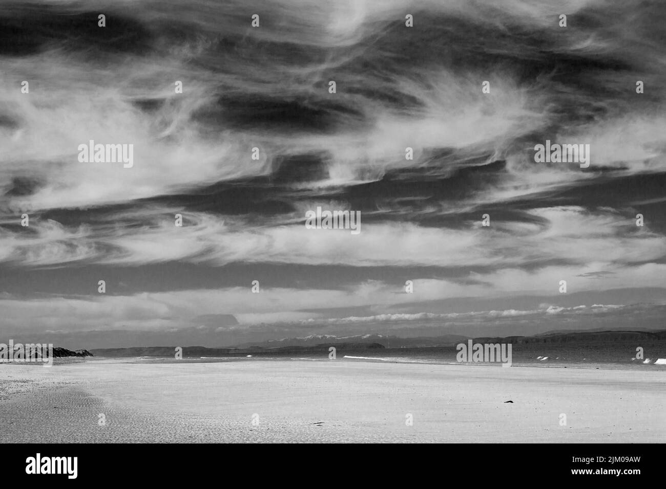 Une vue panoramique d'une plage de sable sur un paysage marin sous un ciel nuageux tourné en niveaux de gris Banque D'Images