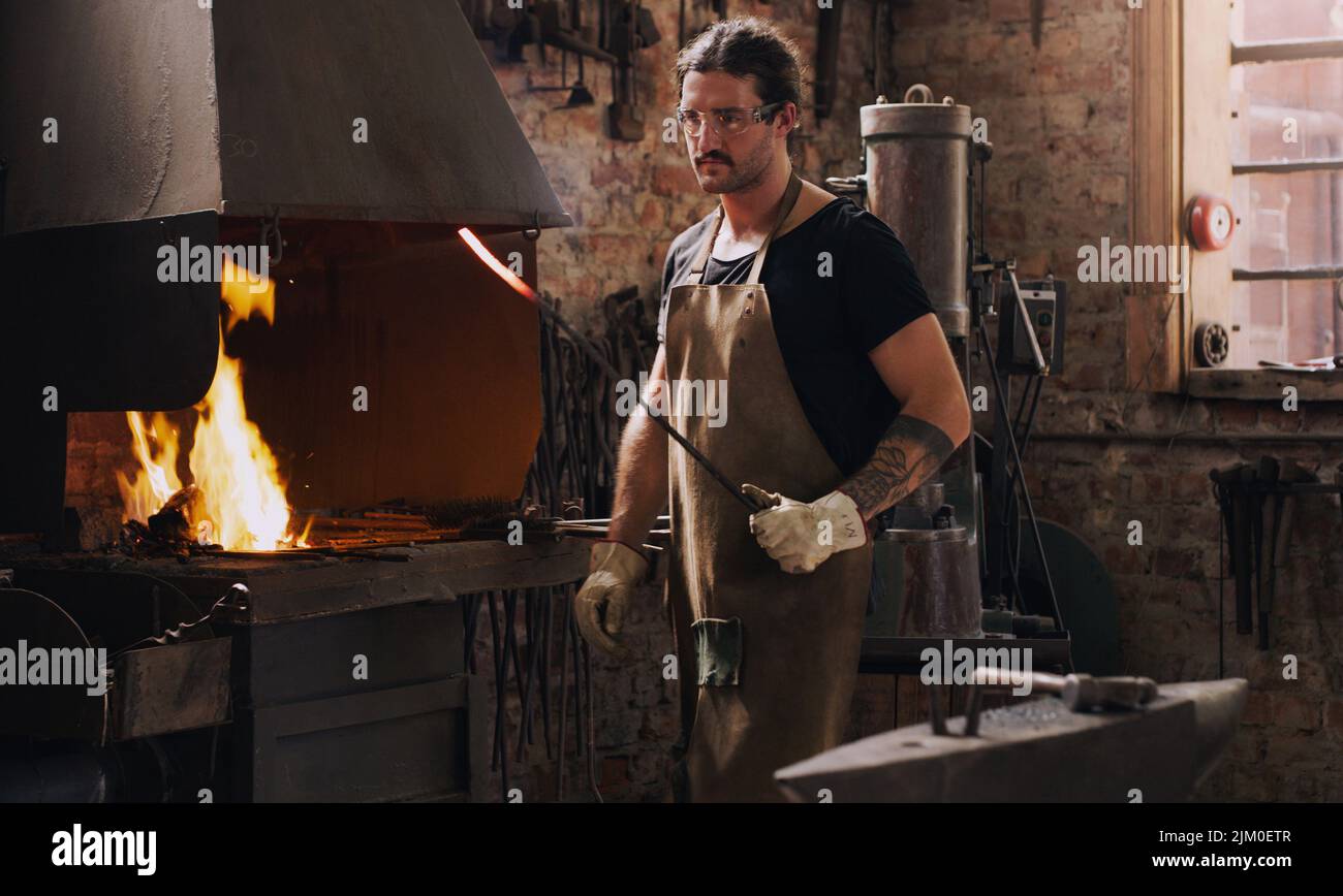 Je crée dans la chaleur du moment. Un homme chauffant une tige métallique dans son atelier. Banque D'Images